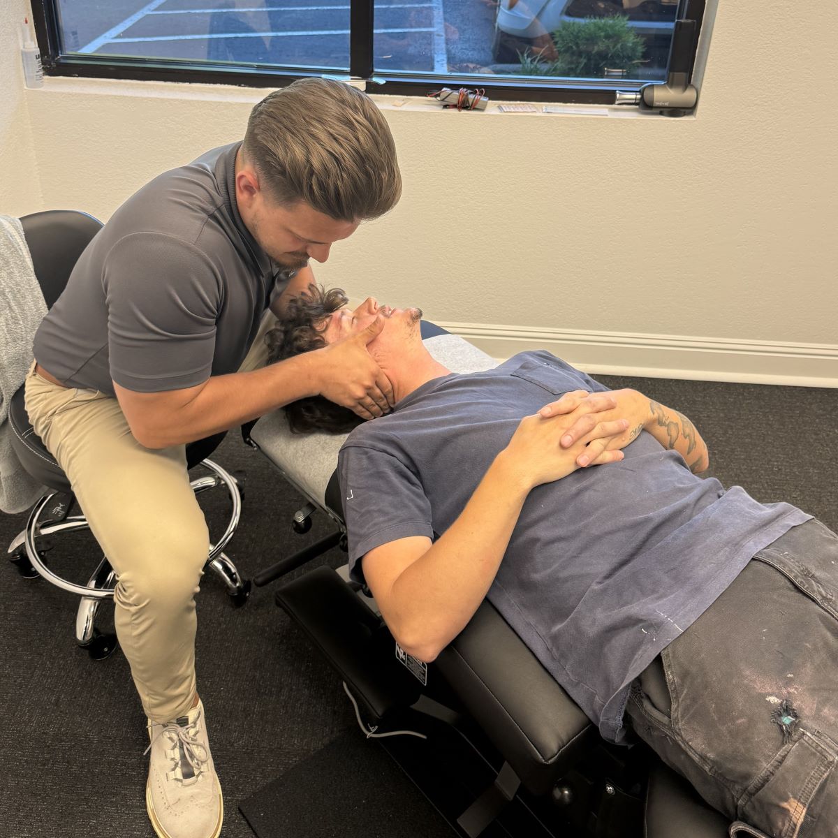 A Sumner chiropractor adjusts a patient's neck while the patient lies on a treatment table in a clinic room.